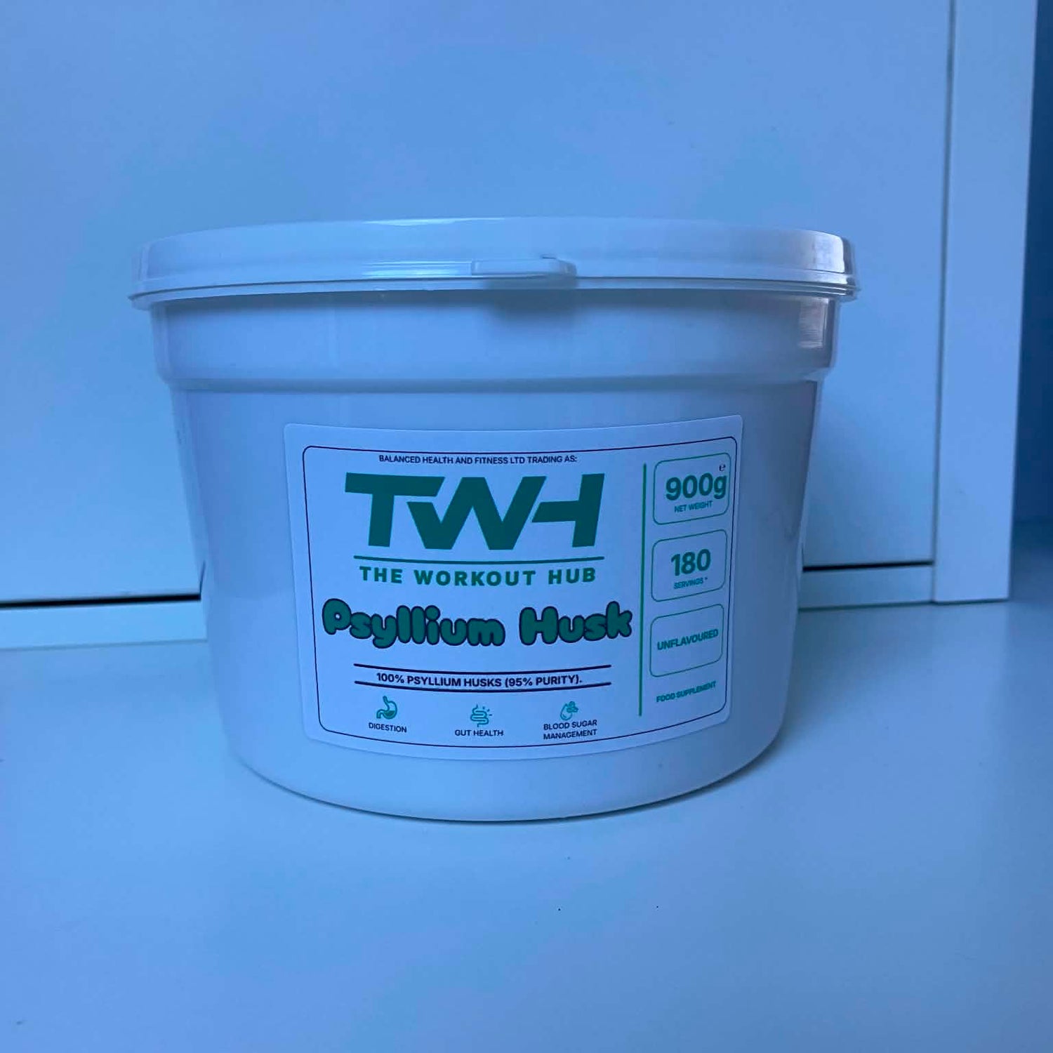 A white plastic tub of TW-H The Workout Hub PayWum Huest 900g supplement powder, photographed on a light blue surface against a matching blue background.